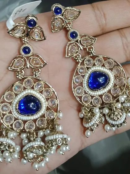 A pair of kundan and jhumki earrings with a striking blue stone in the center.