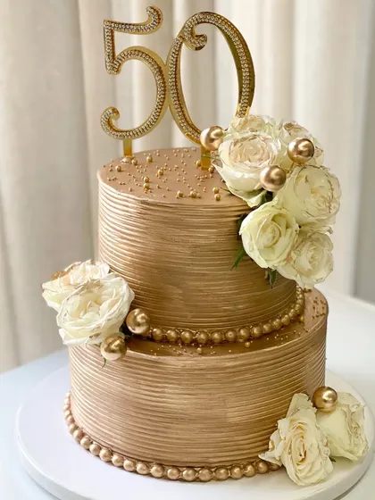 Another view of my signature golden tiered cake, customized for a 50th birthday. The smooth, ribbed ganache finish provides the perfect canvas for the floral arrangements.