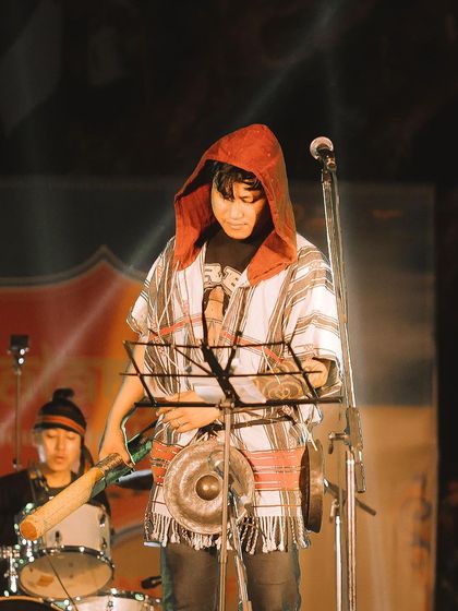 A musician in a hooded poncho plays a traditional instrument on stage. I enjoy capturing the unique styles and instruments of artists from different parts of the country.