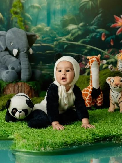 A whimsical jungle adventure. This baby, dressed in a panda costume, explores a lush green landscape filled with friendly stuffed animals.