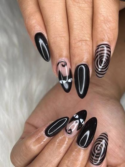 A spooky and fun design. These black stiletto nails feature abstract spiral art and cute cat-eye silhouettes for a unique Halloween-inspired look.