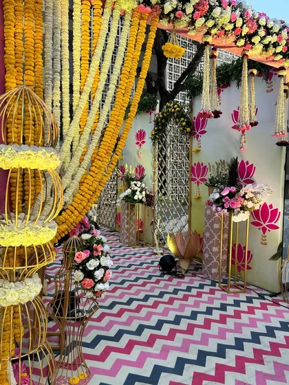 A modern take on Mehendi decor, this entrance features a vibrant pink, black, and white chevron carpet, flanked by traditional marigold strings and contemporary floral arrangements.