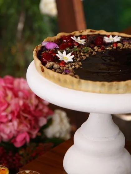 A beautiful chocolate tart on a white pedestal, adorned with fresh berries and edible flowers. We pride ourselves on creating desserts that are innovative, flavourful, and visually indulgent.