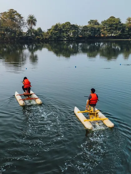 Two people race on water cycles, creating a wake behind them as they pedal across the lake.