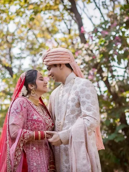 A candid moment of a newlywed couple sharing a look of love amidst lush greenery. The natural outdoor setting provides a soft, romantic backdrop for this authentic interaction.