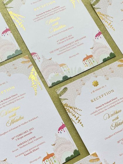 A close-up of the reception cards for the Udaipur wedding, featuring elegant gold foiling over illustrations of palace domes and colorful umbrellas. The details create a sense of royal celebration.