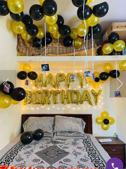 A simple and classic birthday bedroom surprise. The setup includes 'Happy Birthday' foil letters, balloons on the ceiling with hanging photos, and a color theme of black and gold.