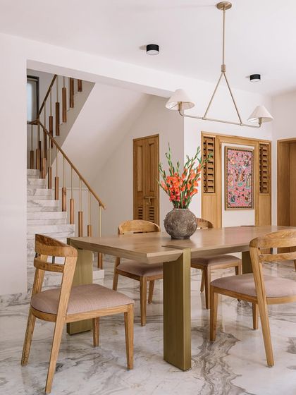 The dining area in Cocoon House is bright and welcoming, set against a backdrop of white marble floors and clean lines. We designed the space with a light wood dining set and a modern chandelier, while a traditional Phulkari artwork adds a touch of color and cultural heritage.