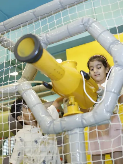 A young explorer peers through a telescope in our play structure, on a mission to spot new adventures.