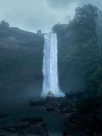 A group of travelers in yellow raincoats stands before a massive waterfall in Meghalaya, a perfect example of the group trips I lead.