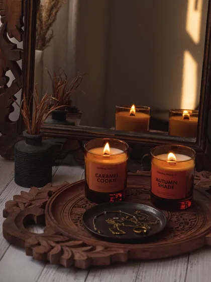 A moody, reflective shot of scented candles on a carved wooden tray. Using a mirror in the styling adds depth and creates an elegant, contemplative atmosphere.