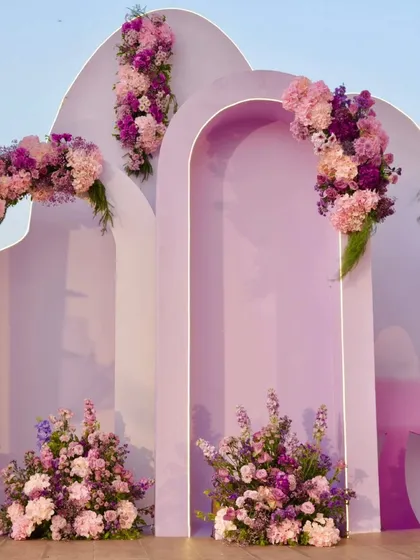 This luxury birthday decor was designed for a baby girl's party. The setup includes custom-shaped backdrops in shades of lavender, accented with beautiful arrangements of purple and pink flowers.