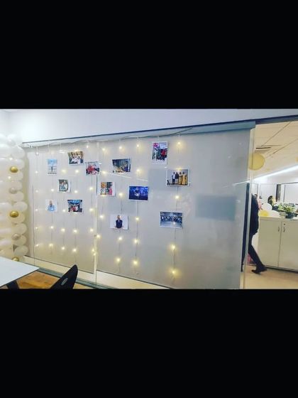 A simple yet heartfelt birthday decoration in an office space, with a wall of photos and fairy lights to celebrate a colleague.