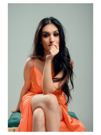 An elegant portrait in a vibrant orange dress. The seated pose is graceful, and the color of the dress stands out beautifully against the muted background.