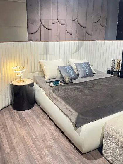 This bed features a tall, winged headboard with vertical channel tufting in a cream-colored fabric. The design creates a grand and luxurious focal point, complemented by a dark, textured wall panel.