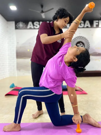 Incorporating light weights to build strength in a modified side-angle pose. The instructor ensures correct form to engage the core and shoulder muscles effectively.