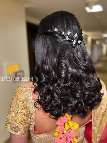A simple and elegant half-up style with a delicate twist and bouncy curls, adorned with small, sparkling clips.