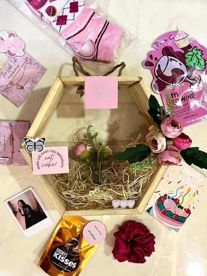 An exploded view of the hexagonal hamper for her. You can see all the individual items like a face mask, Hershey's Kisses, a polaroid photo, and cute socks that go into making this gift special.