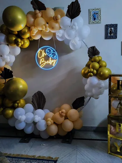 An elegant "Oh Baby" shower setup with a neutral gold, white, and cream balloon ring and matching "BABY" blocks.
