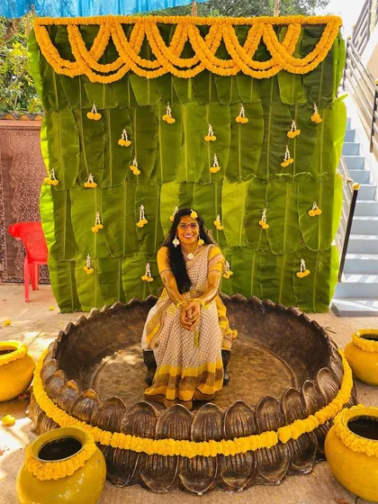 A complete Haldi ceremony setup designed to be both traditional and picture perfect. The backdrop is made entirely of fresh banana leaves, decorated with marigold garlands. We placed a large decorative urli in the center for the ceremony, surrounded by matching yellow pots to complete the vibrant, auspicious theme.