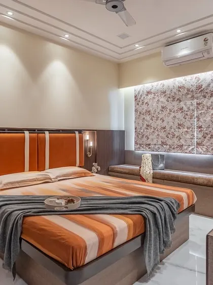 This is a full view of the bedroom featuring a warm orange and wood theme. The custom headboard with integrated sconce lighting, a comfortable window seat, and soft, layered bedding all contribute to a feeling of ultimate comfort and relaxation.