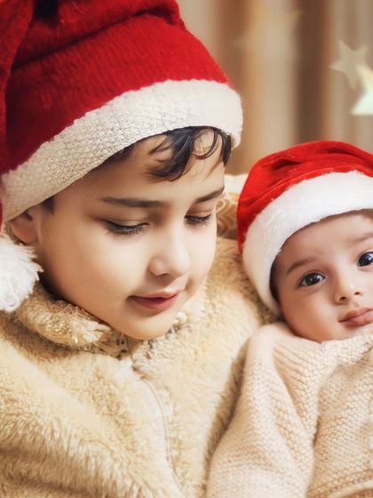 An older brother looks down at his baby sibling during their first Christmas together. This is a tender moment of bonding during a festive family photoshoot.