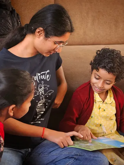 A volunteer reads to two young girls, pointing to the pictures in the book. These one-on-one and small group interactions are crucial for building trust and making each child feel seen and heard.