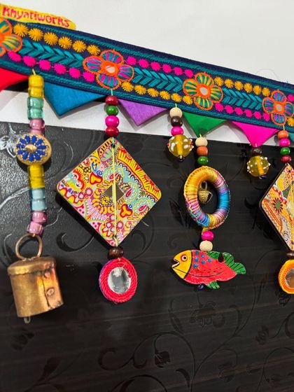 A close-up of 'The Summer Song' toran, showing the detail on the embroidered topper and the hand-painted wooden fish.