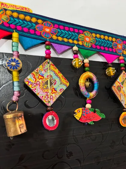 A close-up of 'The Summer Song' toran, showing the detail on the embroidered topper and the hand-painted wooden fish.