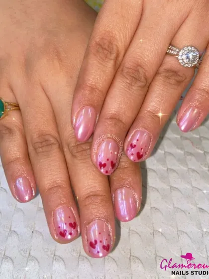 A sweet and shimmery design with a pearlescent pink base and accent nails featuring a scattering of tiny, hand-painted red hearts.