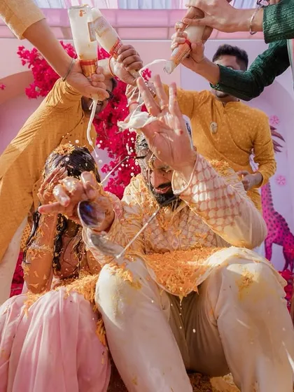The couple getting showered with milk and flower petals during their Haldi, a fun and chaotic moment of celebration.