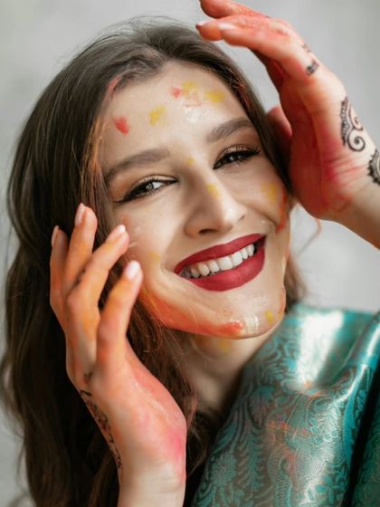 A radiant smile that embodies the happiness of Holi. The vibrant colors on her face and hands tell a story of fun, laughter, and celebration.