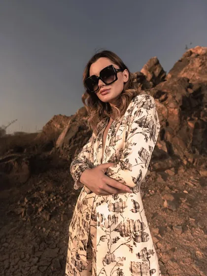 A close-up shot using the natural landscape and a low angle to create a powerful, confident pose. The lighting highlights the model's expression and the texture of the printed blazer.