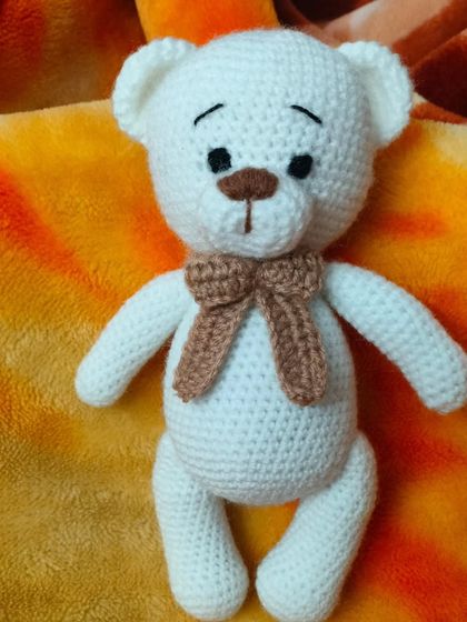 A sweet, handmade white teddy bear with a brown bow. He has a gentle expression and is perfect for comforting hugs.