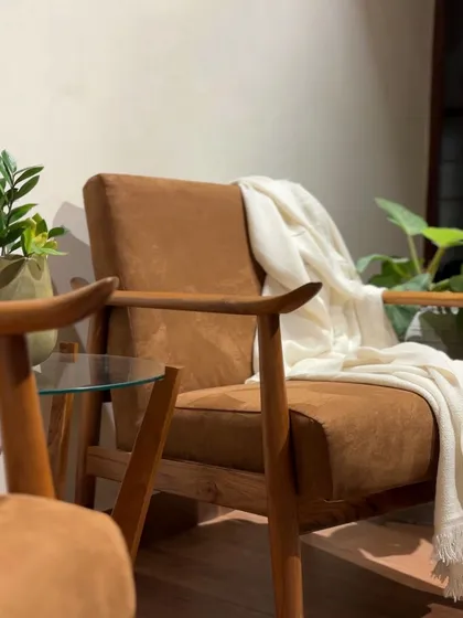 My upholstered armchair in a rich brown fabric, offering a different kind of comfort. The solid teak armrests are sculpted to fit the hand, blending softness with strength.
