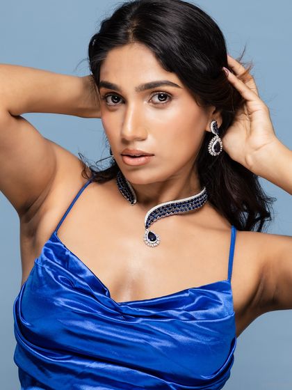 A beauty portrait of a model in a blue satin dress, wearing a sapphire necklace.