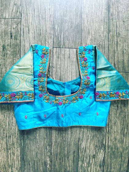 A light blue blouse with floral embroidery on the neckline. The sleeves are made from a contrasting tissue fabric with a Zari border.