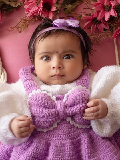 A beautiful close-up of a baby girl in a purple hand-knitted dress, showing off her gorgeous eyes.