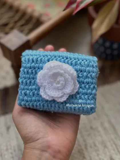 A close-up of the light blue mini wallet featuring a delicate white crochet flower. The craftsmanship in these small details is what makes our products special.