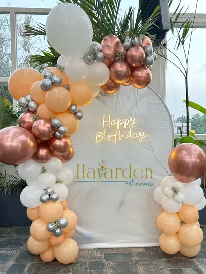 A white arched backdrop with a rose gold, peach, and white balloon garland, creating a soft and elegant look.