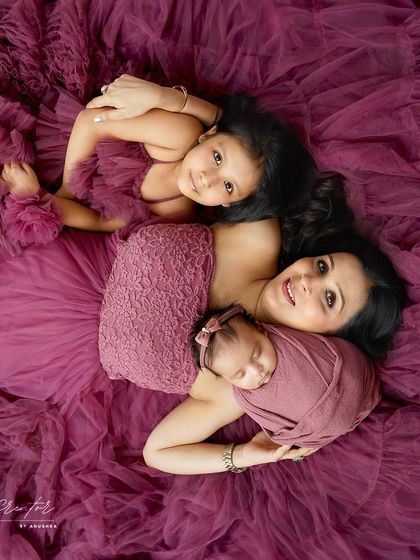 A mother's embrace with her two daughters. This overhead shot shows her holding her newborn while her older daughter snuggles close, all enveloped in a beautiful purple gown.