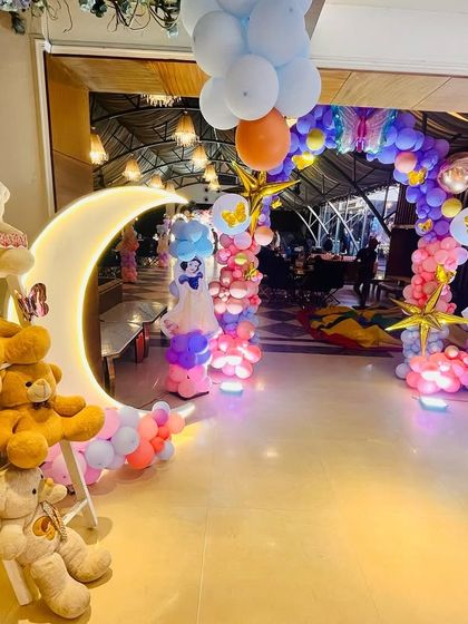 A creative fairy theme entrance with a moon-shaped prop, teddy bears, and a balloon archway to welcome guests.