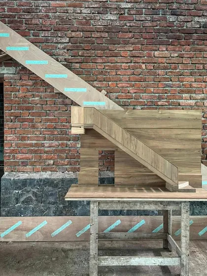 A 1:5 scale model of a staircase, meticulously crafted from wood, sits on a workbench against a brick wall. This model serves as a three-dimensional drawing for the artisans who will build the full-size version.