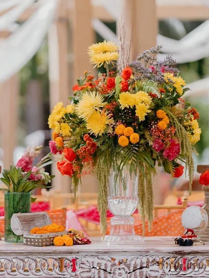 A stunning floral centerpiece featuring a mix of yellow chrysanthemums and other colorful blooms, surrounded by smaller decor elements.