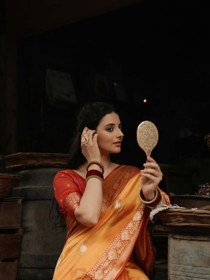 A candid moment of adjustment, this portrait captures the model arranging her hair while looking in the mirror, adding a touch of realism to the traditional scene.