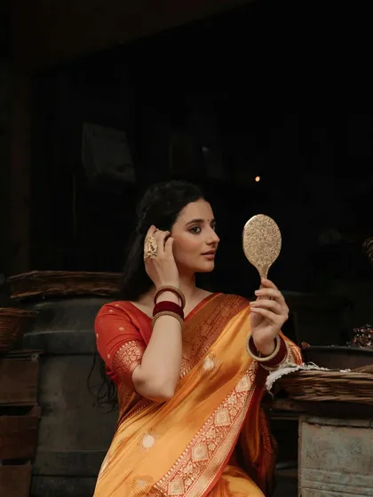 A candid moment of adjustment, this portrait captures the model arranging her hair while looking in the mirror, adding a touch of realism to the traditional scene.
