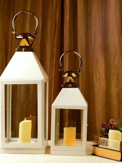 Two white lanterns of different sizes are styled together for a clean and modern home decor shot. The warm candlelight inside provides a beautiful contrast to the crisp white frames.