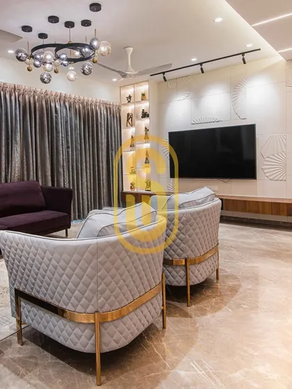 A different perspective of the living room, highlighting the quilted grey armchairs with gold-finished frames. This view shows the relationship between the seating arrangement and the custom TV wall unit.