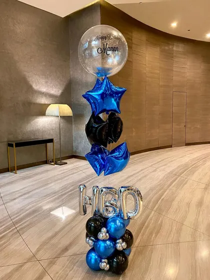 A stylish blue and black balloon bouquet for a birthday. This arrangement features a personalized bubble balloon at the top, with foil stars and latex balloons layered for a tall, impressive look.