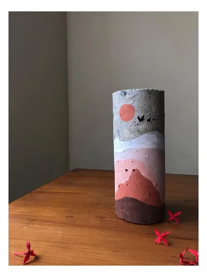 A close-up of the day-themed concrete sculpture. The earthy tones and simple depiction of a sun and birds create a warm, serene feeling. This hand-painted art piece is a perfect example of sustainable home decor.